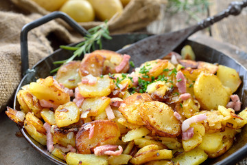 Deftige Bratkartoffeln mit Speck und Zwiebeln rustikal in der Eisenpfanne serviert – Hearty fried potatoes with onions and bacon served in an iron pan
