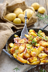Deftige Bratkartoffeln mit Speck und Zwiebeln rustikal in der Eisenpfanne serviert – Hearty fried potatoes with onions and bacon served in an iron pan