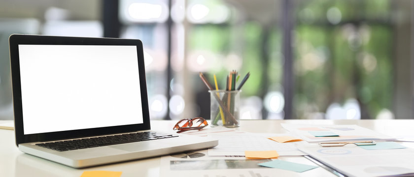 Business workspace with computer laptop blank screen is putting on a desk surrounded by various equipment.