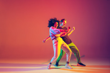 Drive in motion. Stylish man and woman dancing hip-hop in bright clothes on green background at...