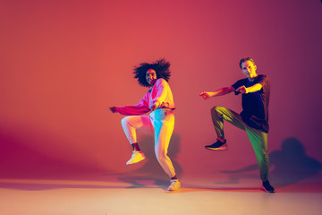 Drive in motion. Stylish man and woman dancing hip-hop in bright clothes on green background at...