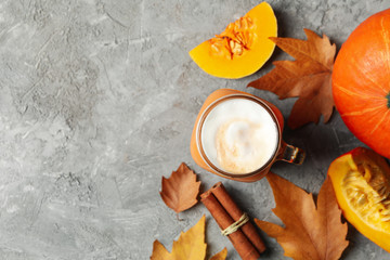 Composition with pumpkin latte, pumpkin, leaves and cinnamon on gray table