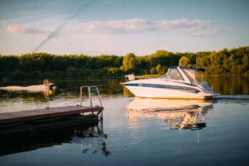 Pleasure boat sails near the pier on tranquil lake or river. Summertime landscape photography