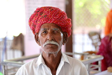 Old Indian man in long white mustache and wearing red turban suffering from eye problem. Cataract...