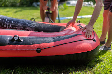 Red rubber boat is inflated with a hand pump and checked by two young men. Close-up on green grass...