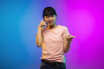 Need you to call. Asian young woman's portrait on gradient studio background in neon. Beautiful female model in casual style. Concept of human emotions, facial expression, youth, sales, ad.