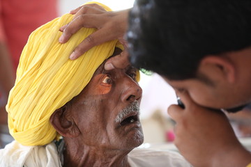 Old Indian man in Yellow turban from Rajasthan getting eyes tested. Eye camp. Eye patient. Weak eyesight. Eye Health. Eye examination by doctor. Healthcare to elderly.