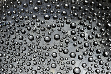 Silver drops flow down on the gray mirror ice surface. Close-up.