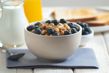 Breakfast with granola and blueberry, milk with orange juice and baked toasts on the white wooden table close-up