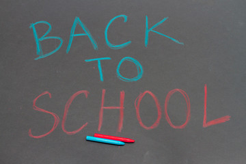 Fototapeta na wymiar Inscription back to school on black chalkboard. Colored crayons on school black board