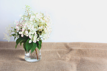 bouquet in a glass vase on a jute cloth. beautiful white hydrangeas