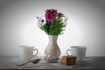 On the table is a vase of flowers. Next to her mugs for tea, sugar, cookies. Everything is ready for tea