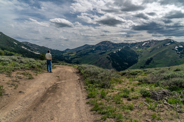 Fototapeta na wymiar A man standing on a dirt road, path, watching a scene of distance mountains and dramatic clouds in the sky, Bear Creek Summit, Jarbidge, Nevada