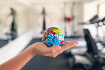 Toy globe in the female hand in fitness gym opposite the sport equipment and  jogging simulators. Healthy lifestyle. World health day. concept.