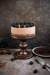 Chocolate mousse cake with blackberries on a high wooden stand. Lots of berries. A slice of cake on a plate. Still life with dessert. Festive dinner.