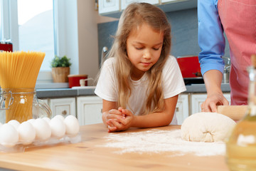 Little daughter helping her mom kneading dough