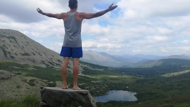 man stands on top of a mountain with open hands. at the top of the mountain, a man with his arms spread wide.