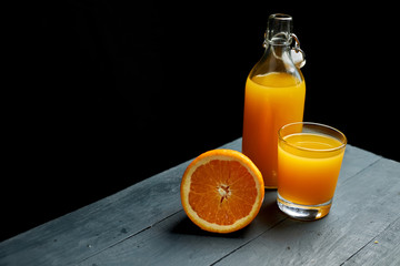 orange juice in a bottle and glass on a wooden table with fresh fruit against black background