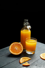 orange juice in a bottle and glass on a wooden table with fresh fruits against black background