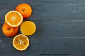 Glass of orange juice on wooden table with fresh sliced fruits of orange. Free space for your text. Top view.