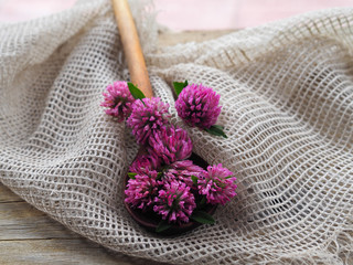 Useful plant trifolium with crimson flowers and a wooden spoon with clover on a wooden background, top view. Therapeutic flowers for use in alternative medicine and cosmetology