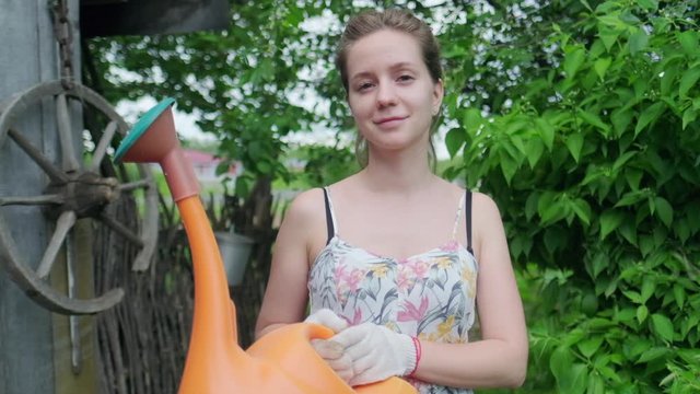 Lady in the garden. Young adult woman stands in the summer garden with watering can and looks at the camera