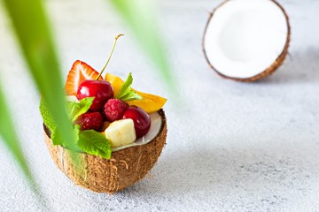 Fruit salad in a bowl of half coconut on a gray background with a place for text, copy space. Healthy natural organic food, low calories delicious dessert.