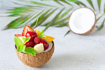 Fruit salad in a bowl of half coconut on a gray background with a place for text, copy space. Healthy natural organic food, low calories delicious dessert.