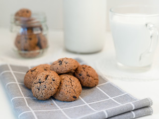 homemade oatmeal cookies with cracks and pieces of chocolate on a gray napkin, a cup of milk and a glass bottle - breakfast