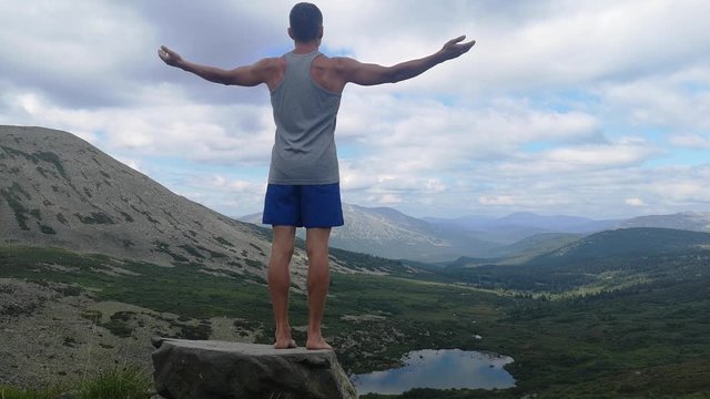 man stands on top of a mountain with open hands. at the top of the mountain, a man with his arms spread wide.