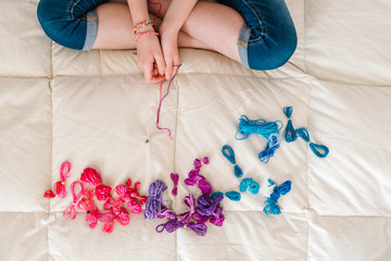 horizontal image seen from above of a girl's hands making colored bracelets.