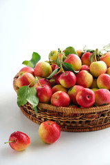 Red and yellow ripe apples with leaves close-up in a wicker basket on a light background. Close up. No people