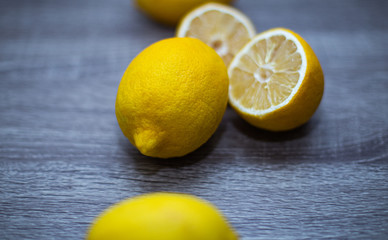 Three whole lemons lie in a row on a wooden table, next to the middle lemon another lemon - cut in half