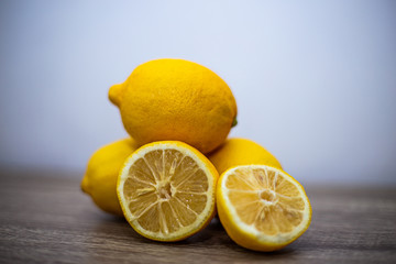 Three whole lemons lie on top of each other, in the foreground two halves of a sliced fourth lemon in the middle