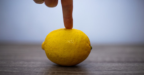 One lemon is lying on the table, the fruit is holding the index finger of a man's hand, the other fingers are clenched into a fist