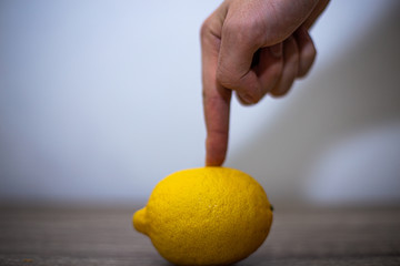 One lemon is lying on the table, the fruit is holding the index finger of a man's hand, the other fingers are clenched into a fist