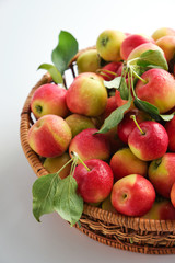 Red and yellow ripe apples with leaves close-up in a wicker basket on a light background. Close up. No people