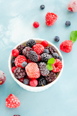 Mix of summer frozen berries in a white bowl on a blue concrete background. Copy space.