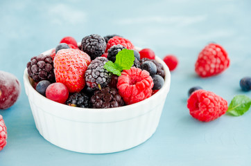 Mix of summer frozen berries in a white bowl on a blue concrete background. Copy space.
