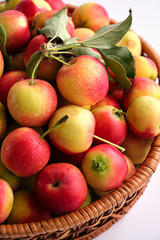 Red and yellow ripe apples with leaves close-up in a wicker basket on a light background. Close up. No people