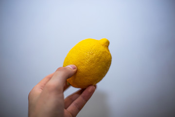 Male fingers holding a lemon on a white wall background