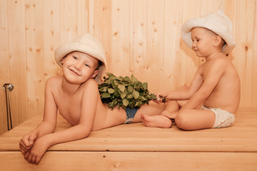 Two little boy, with bath hats on their heads and turned into white sheets looking on each other,...