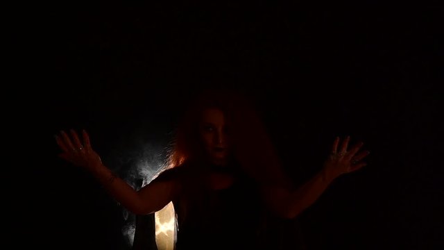 A witch with long curly hair holds a magic fire. Tongues of flame on the palms of a red-haired woman.