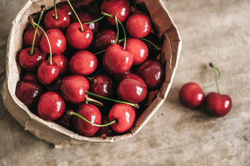 Fresh ripe cherries in a paper bag on wooden background. Top view. Copy, empty space for text