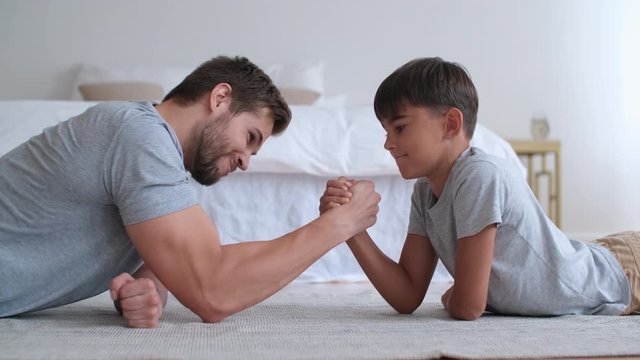 Family fitness at home, Father coach, Sports kid, Fun gymnastics. Cheerful dad and son are fighting with their hands while lying on the floor at home