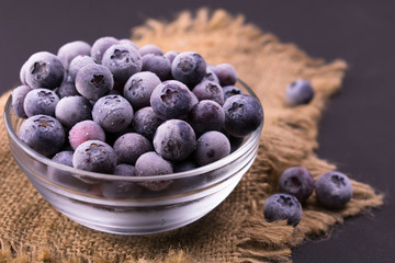 
Frozen blueberries in a transparent plate on a black background.
Close-up.