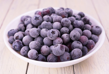 
Plate with frozen blueberries on a wooden white background.
Close-up.