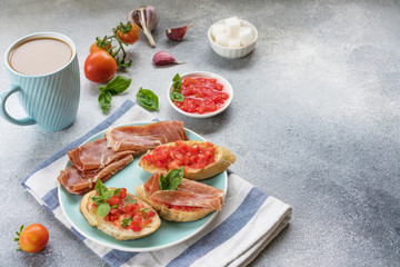 bruschetta, toast with sliced tomatoes, jamon and Basil on a blue plate, and coffee with milk in a blue Cup. copy space