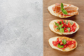 bruschetta, toast, with sliced tomatoes, jamon and Basil on a wooden chopping Board. copy space, flatly