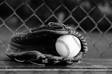 Baseball in ball glove close up, sitting on dugout bench for game in black and white.